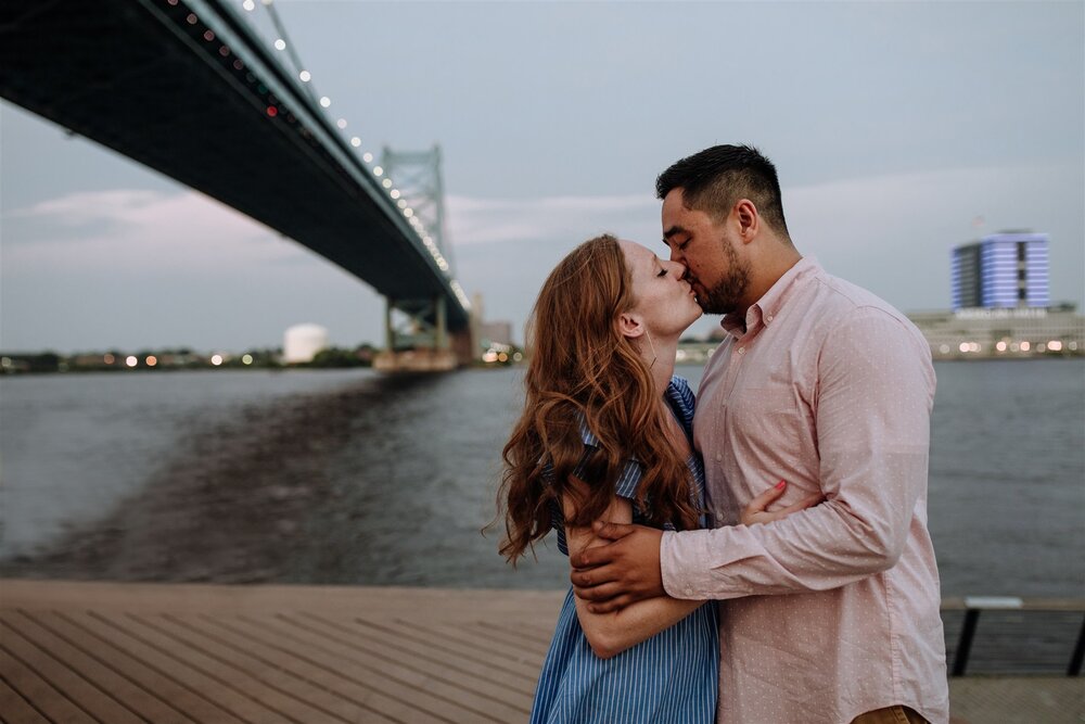 A man and woman kiss in front of a bridge in Philadelphia, PA