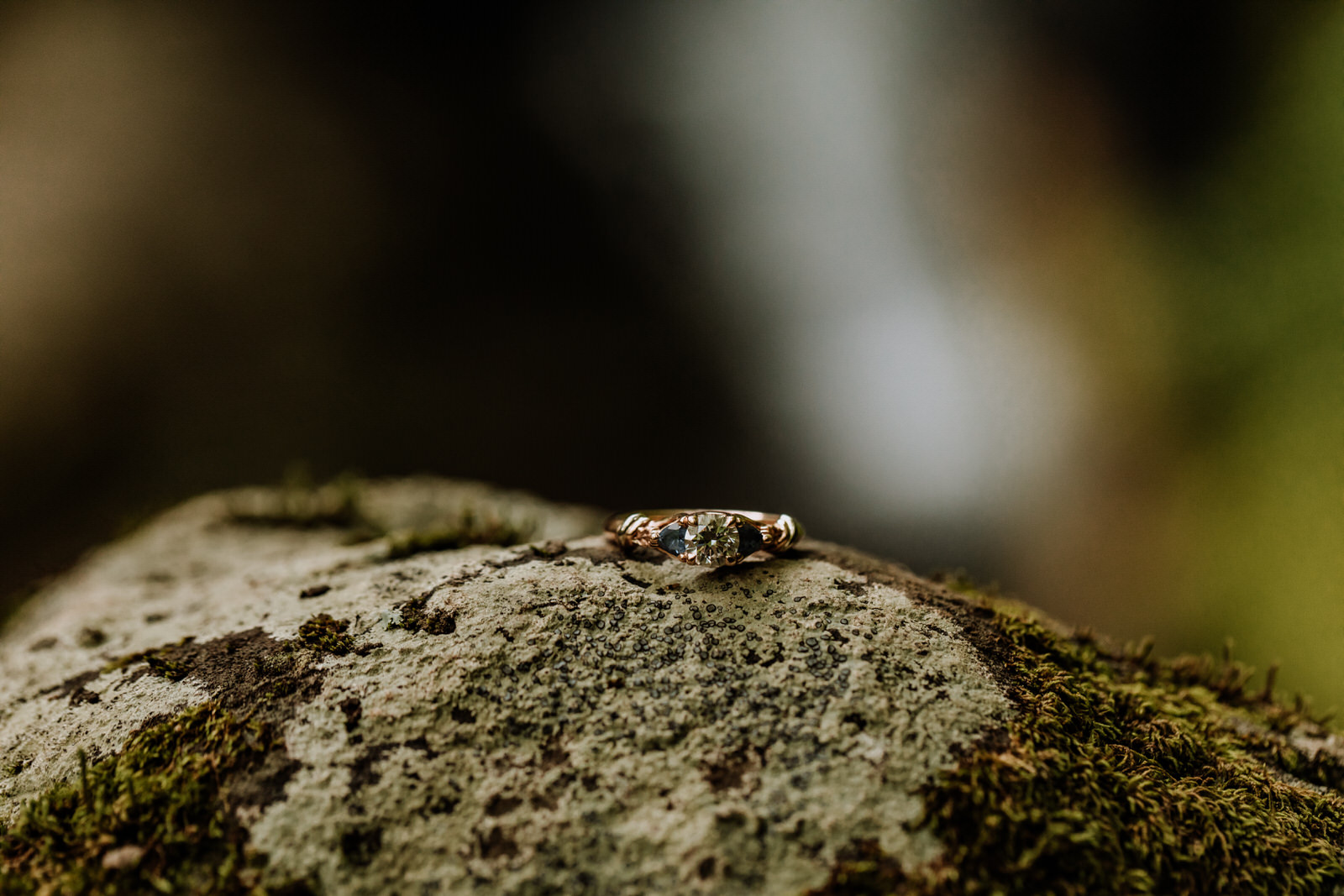 Close up of an engagement ring on a rock with moss