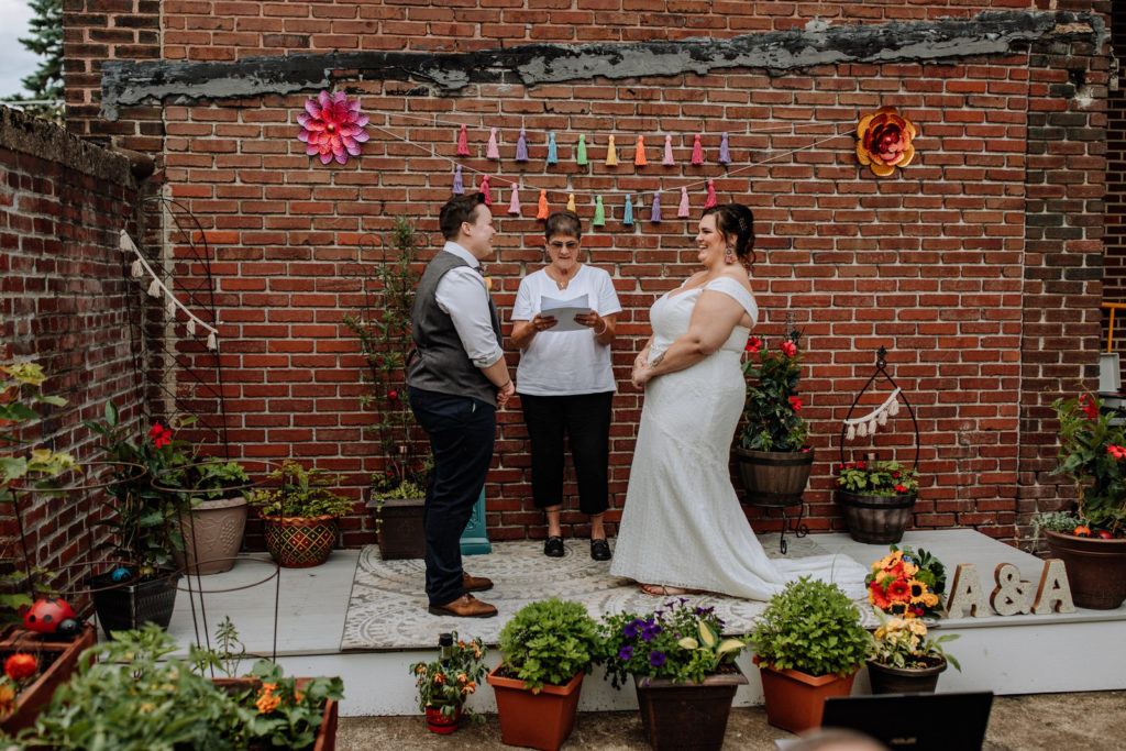 Two women married in their backyard patio in front of a brick wall, standing on a wooden platform. 