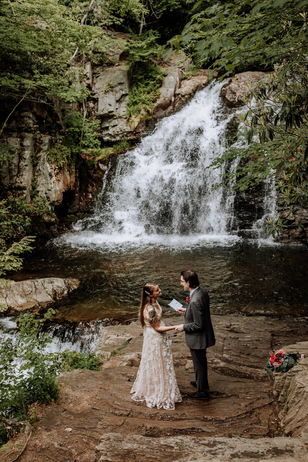 Man and woman reading vows during wedding ceremony in front of a waterfall