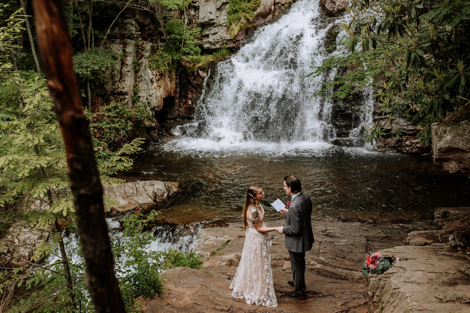 Man and woman reading vows during wedding ceremony in front of a waterfall