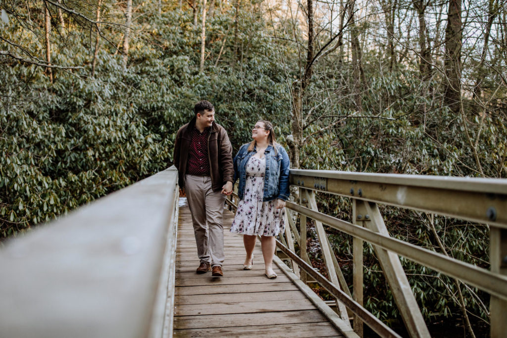 Man and woman holding hands and walking on a bridge in the woods