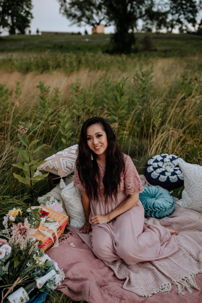 Portrait of a woman sitting comfortably on a collection of blankets and pillows in a grassy field