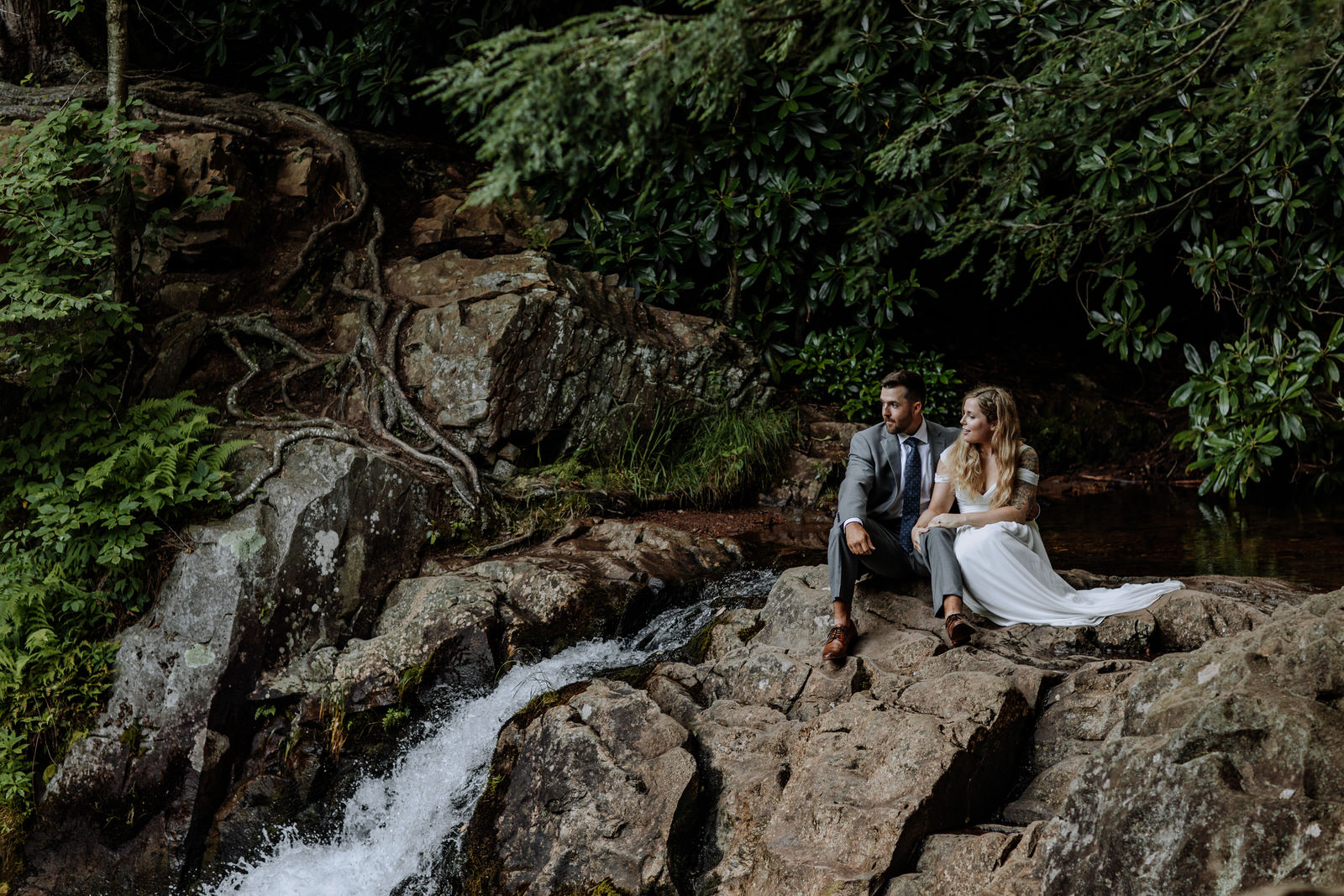 Man and woman dressed up in wedding attire sitting on top of waterfall in Hickory Run State Park