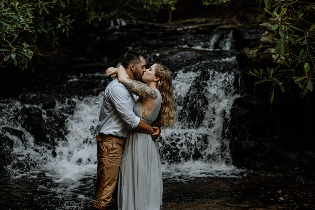Man and woman kissing in front of a waterfall, in the water