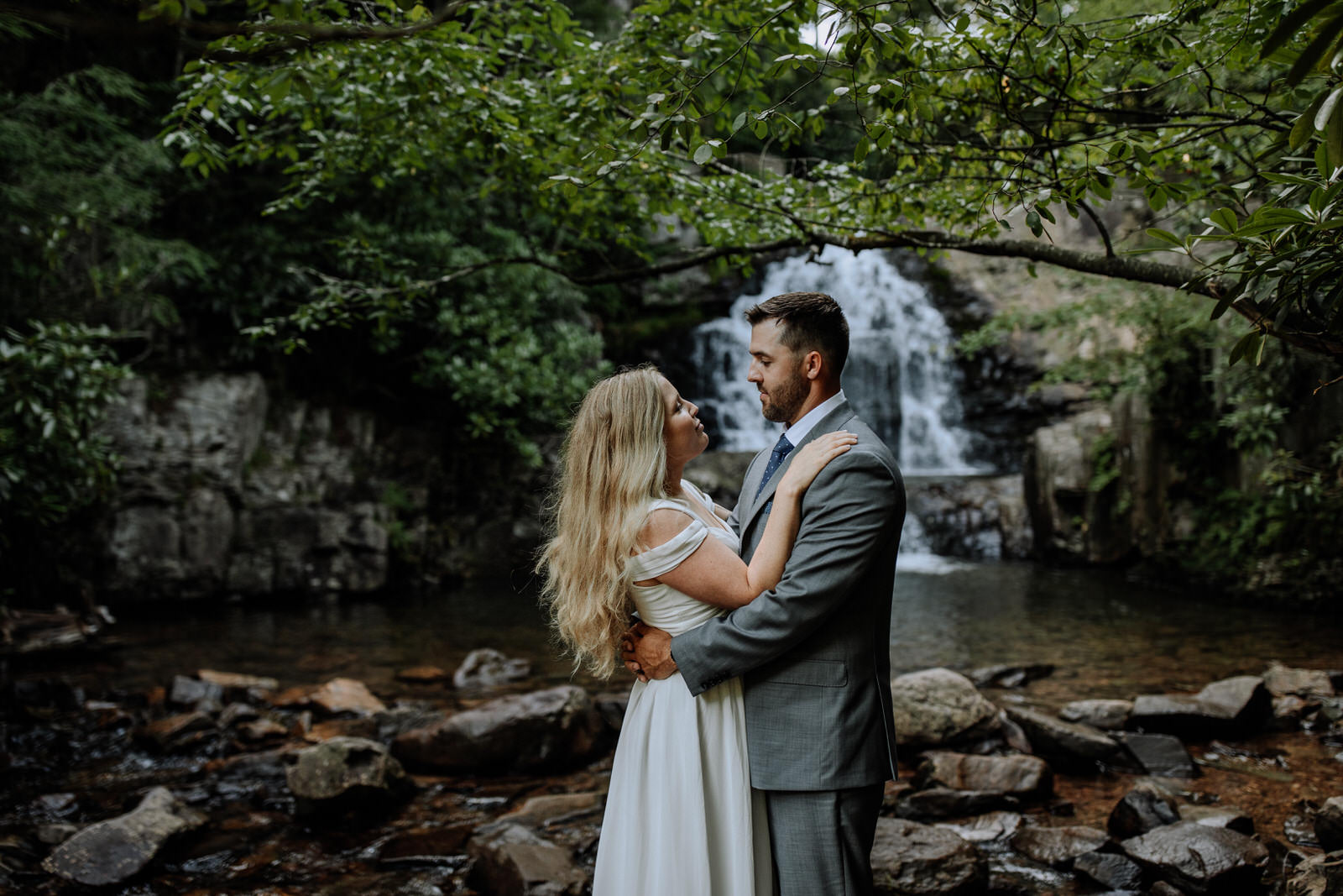 Man and woman dressed up in wedding attire looking at each other in front of Hawk Falls in Hickory Run State Park