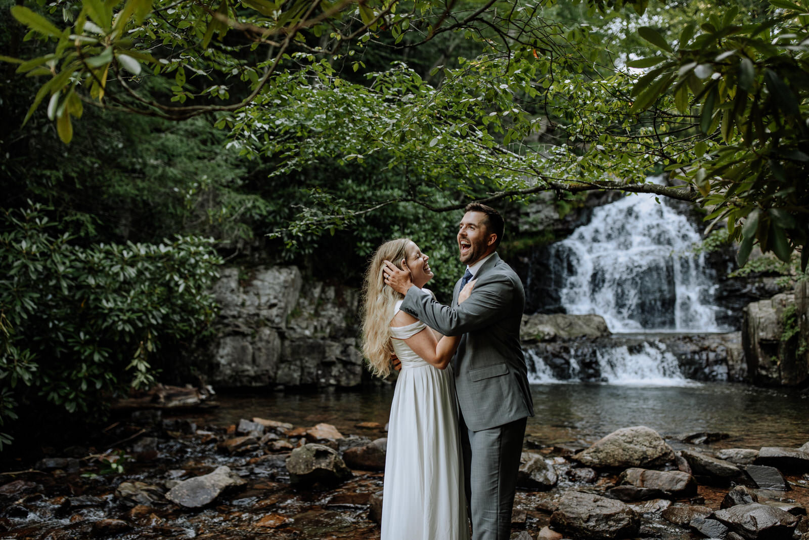 Man and woman dressed up in wedding attire laughing in front of Hawk Falls in Hickory Run State Park