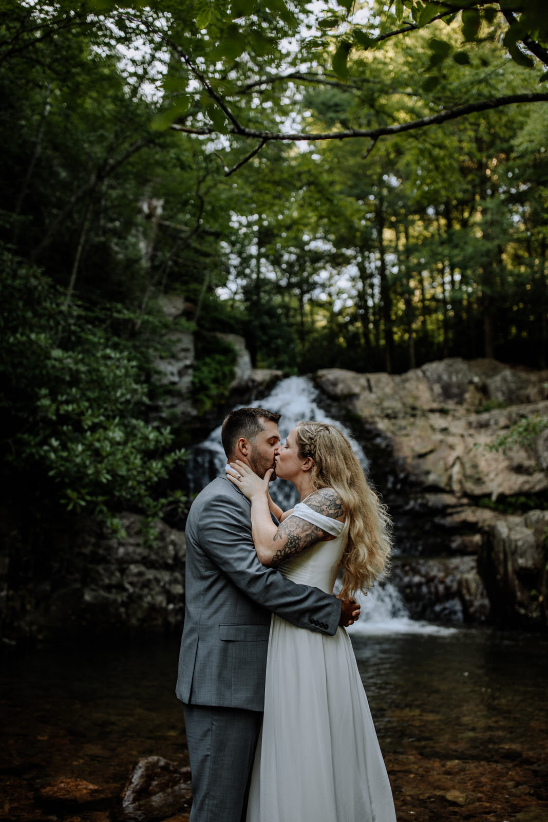 Man and woman dressed up in wedding attire kissing in front of Hawk Falls in Hickory Run State Park
