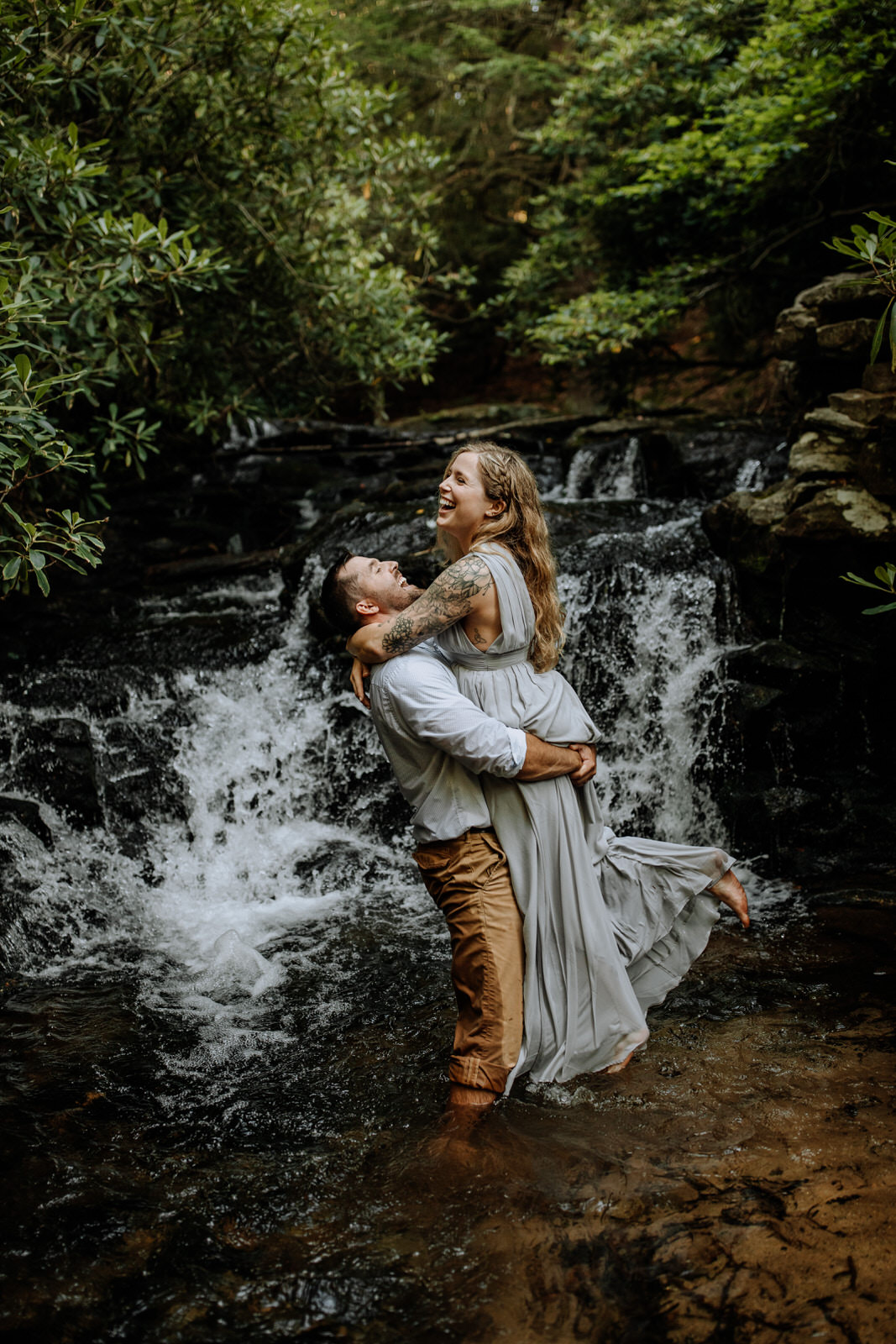 Man picking up a woman and both laughing in front of a waterfall