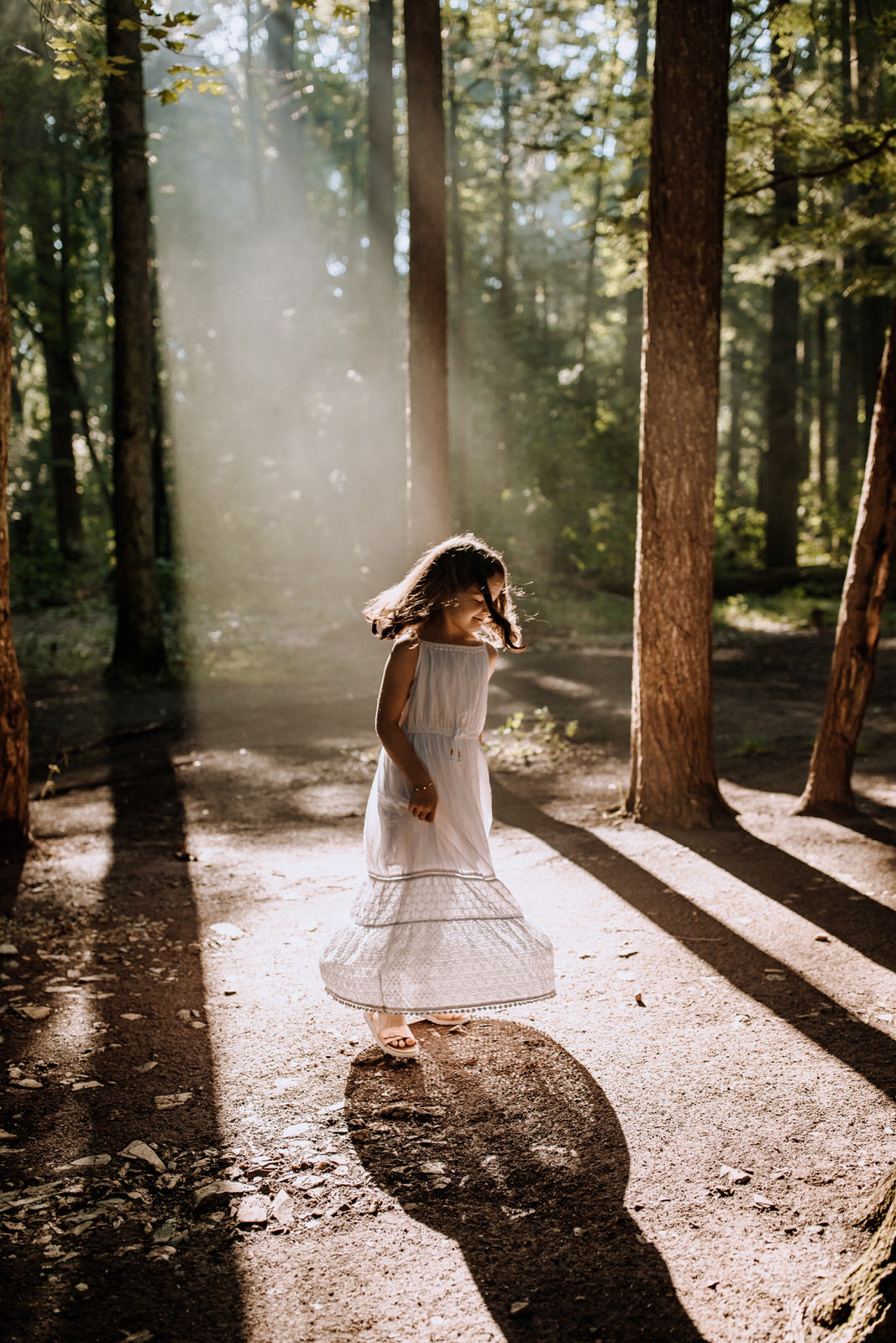 Young girl dancing in a dress in a beam of sunlight in the woods