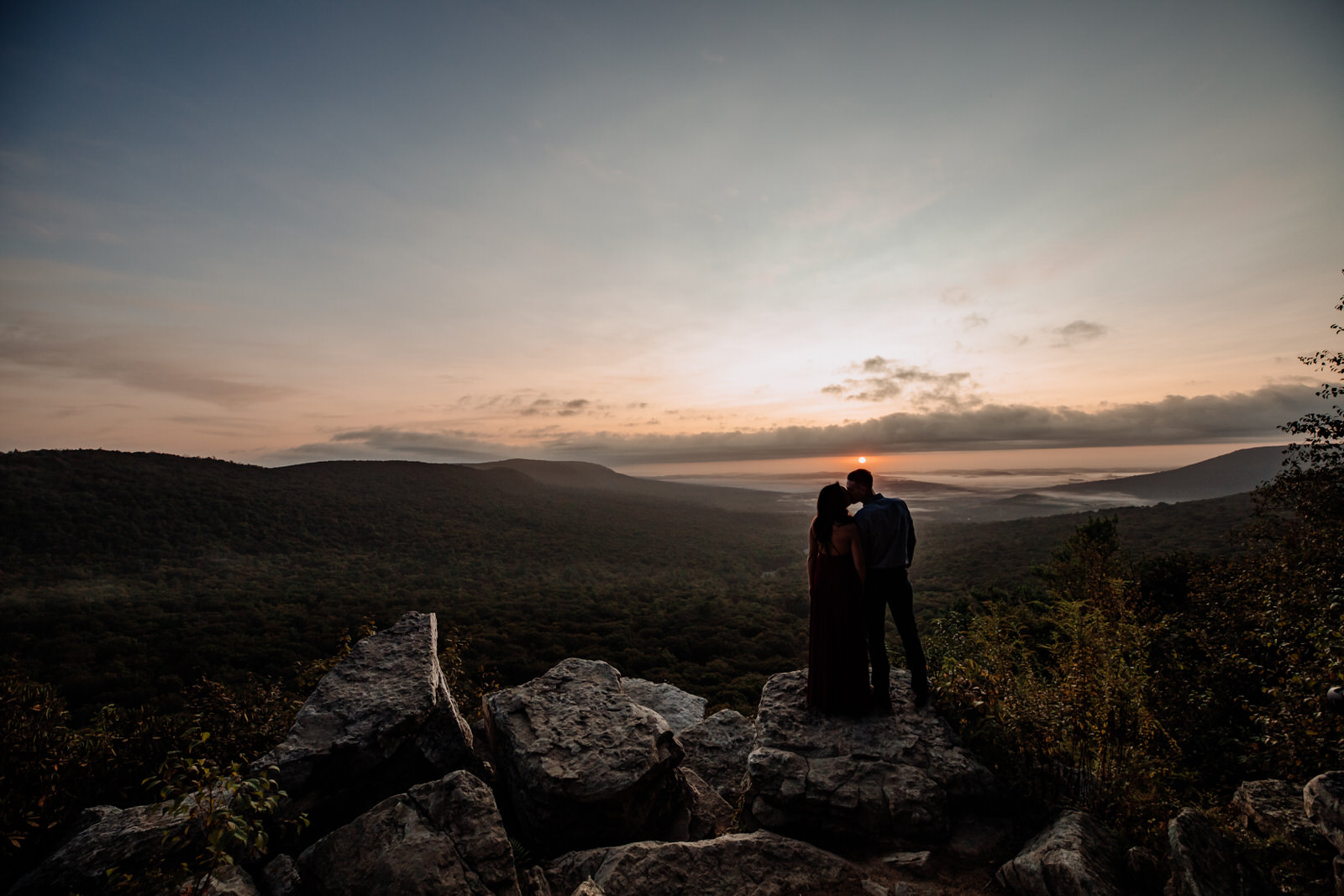 Sunrise engagement picture taken at Hawk Mountain (Kempton, PA). Couple seen silhouetted kissing with large landscape in background.