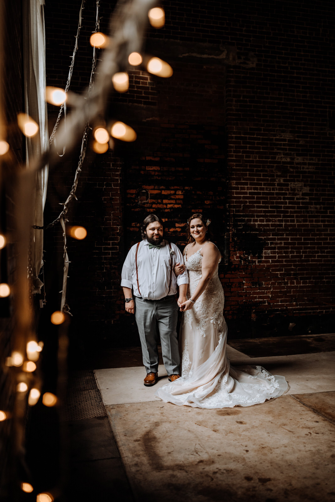 Bride & Groom Portrait in front of a brick wall with window light with string lights