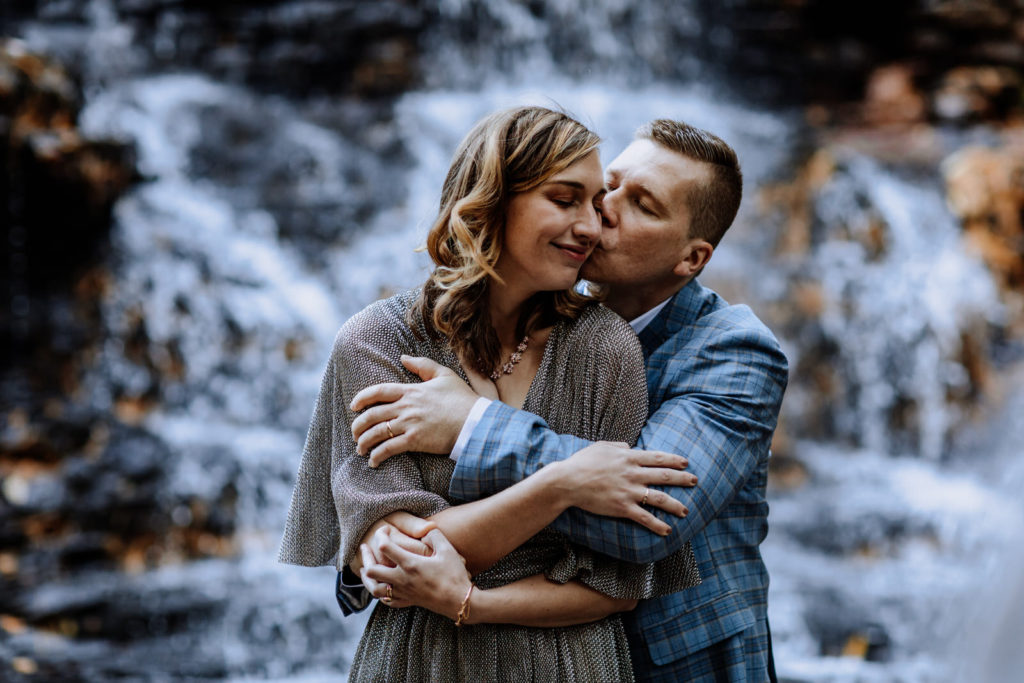 Man and woman holding each other and kissing in front of a waterfall during their elopement in Pennsylvania