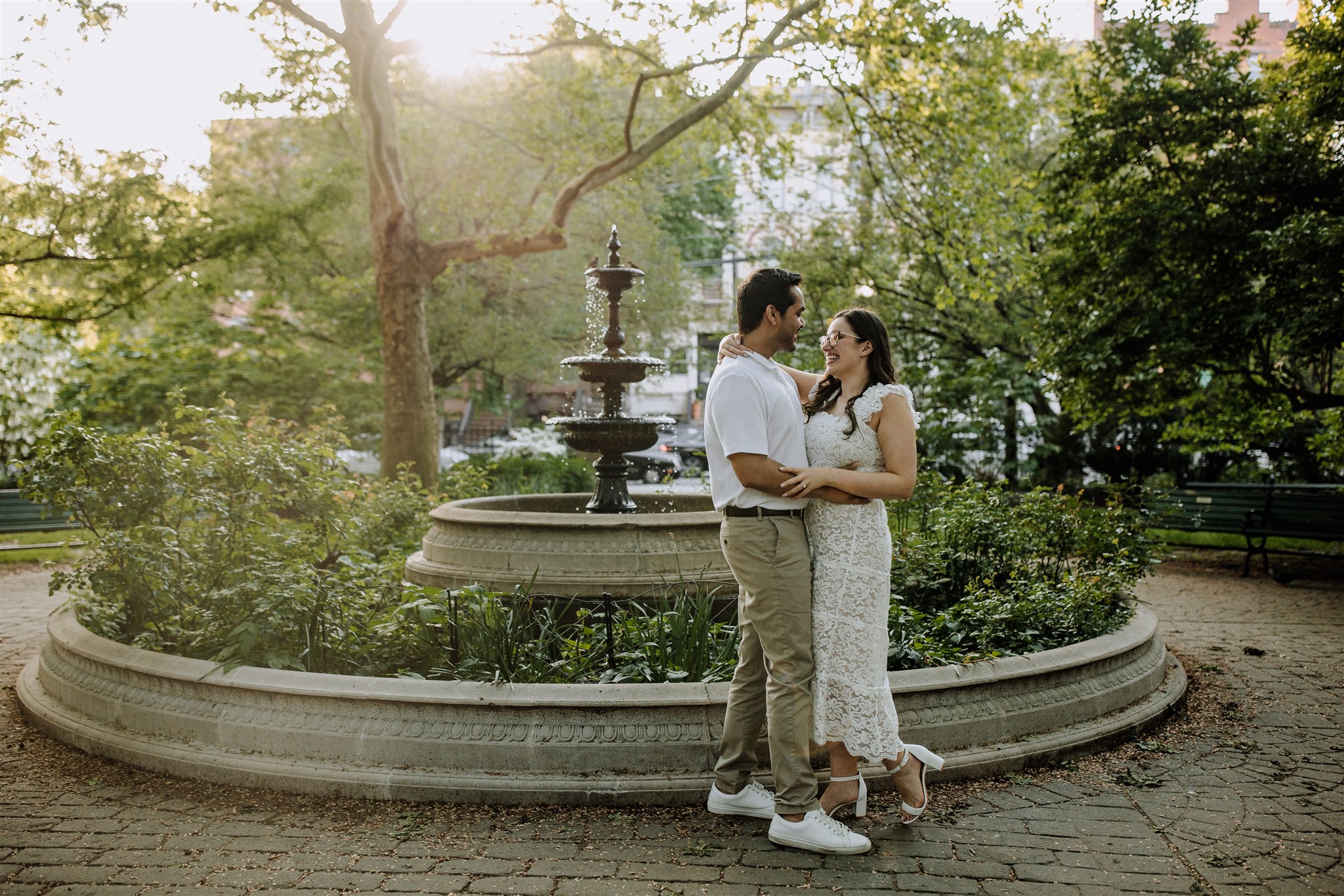 Man and woman holding each other in front of a fountain in Van Vorst Park in Jersey City, NJ.